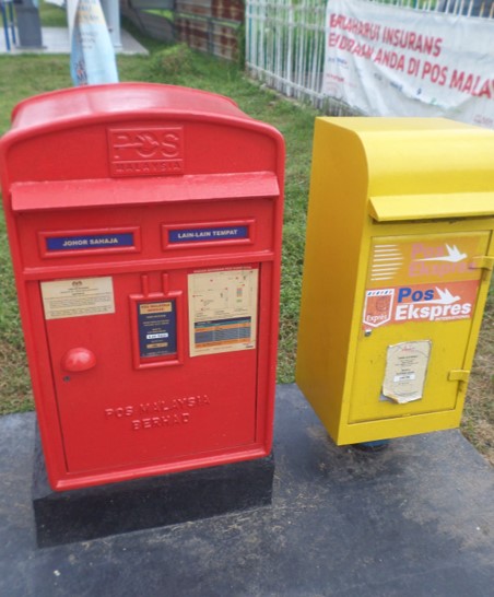 Red and yellow mailboxes next to each other on the street. 