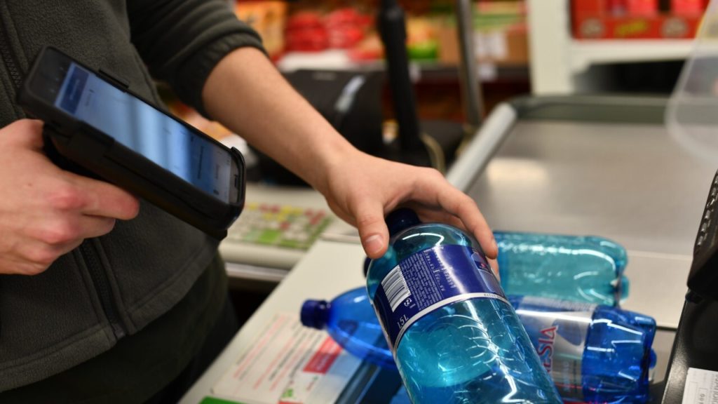 A man holding a hand scanner and scanning the EAN code of bottle. 