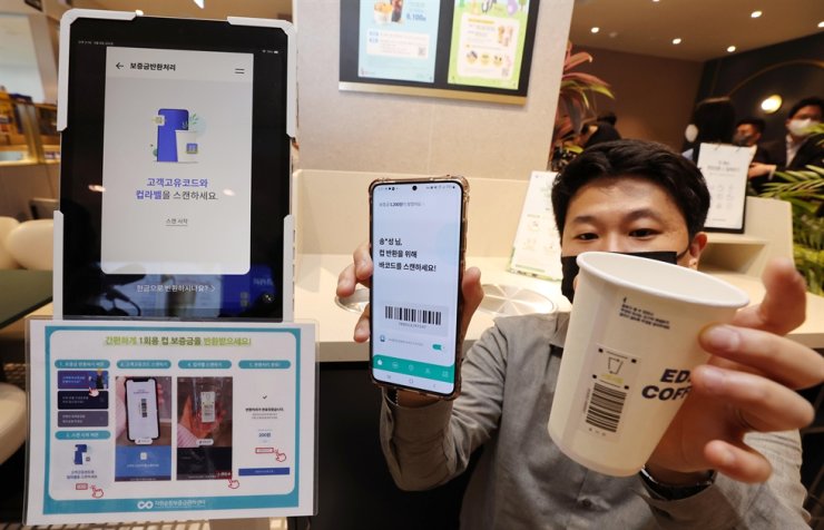 A teenage boy holding a coffee cup in one hand and in the other phone with scanned EAN code from the cup. 