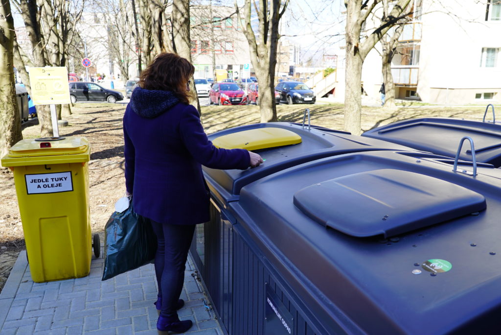 A lady who is opening the semi-underground bin with a chip to throw trash away.