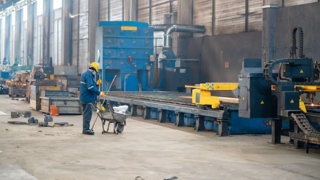 Worker with a wheelbarrow standing in the production hall of the factory cleaning the working area.