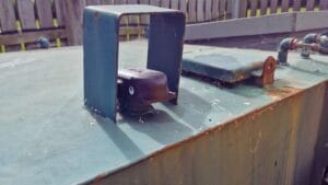 Small sensor mounted on a metal container, protected by a rusted metal hood.