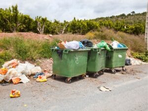 Overflowing green trash bins with scattered garbage on the ground.
