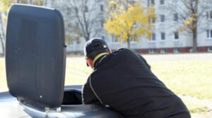 A person opening a waste bin to dispose of trash, likely in a public area.
