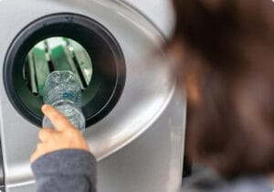 A person inserting a plastic bottle into a recycling machine.
