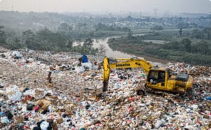 A waste landfill with plastic trash and an excavator working to manage it.