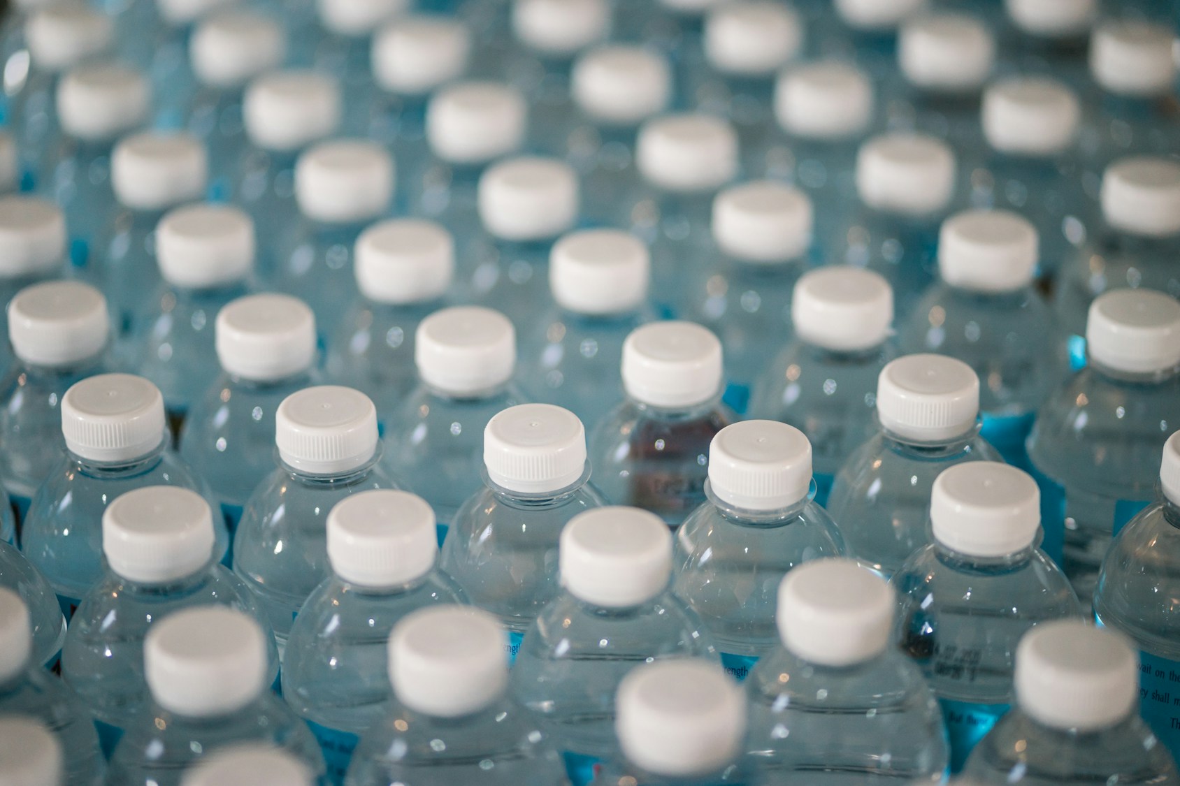 Numerous plastic water bottles with white caps arranged in a grid.