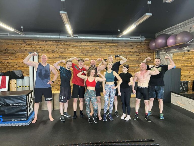 Group of people flexing and smiling after a workout in a gym.