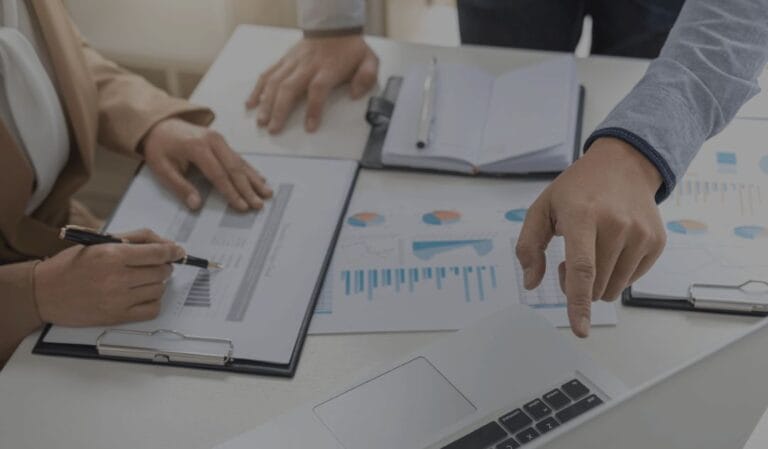 People reviewing charts and pointing at data on a laptop and documents.