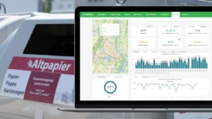 Laptop shows waste-analytics dashboard with bin fill data and a map, placed beside a paper recycling container.