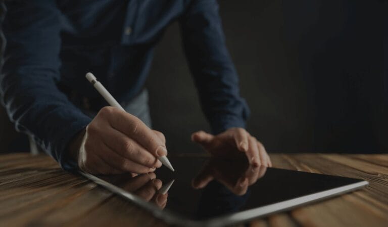 Person writing on a tablet with a stylus on a wooden table.
