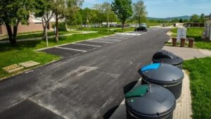 Several large outdoor waste containers beside a paved parking area.