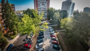 Parking area with cars and smart underground waste bins surrounded by tall residential buildings and trees.