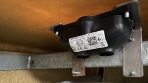 A mounted black Sensoneo sensor unit fixed to metal brackets beneath a flat surface.