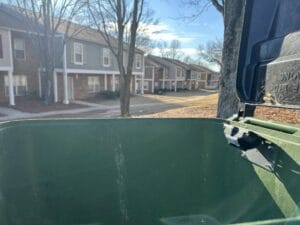 An outdoor recycling bin with a fill-level sensor installed, overlooking nearby residential buildings.