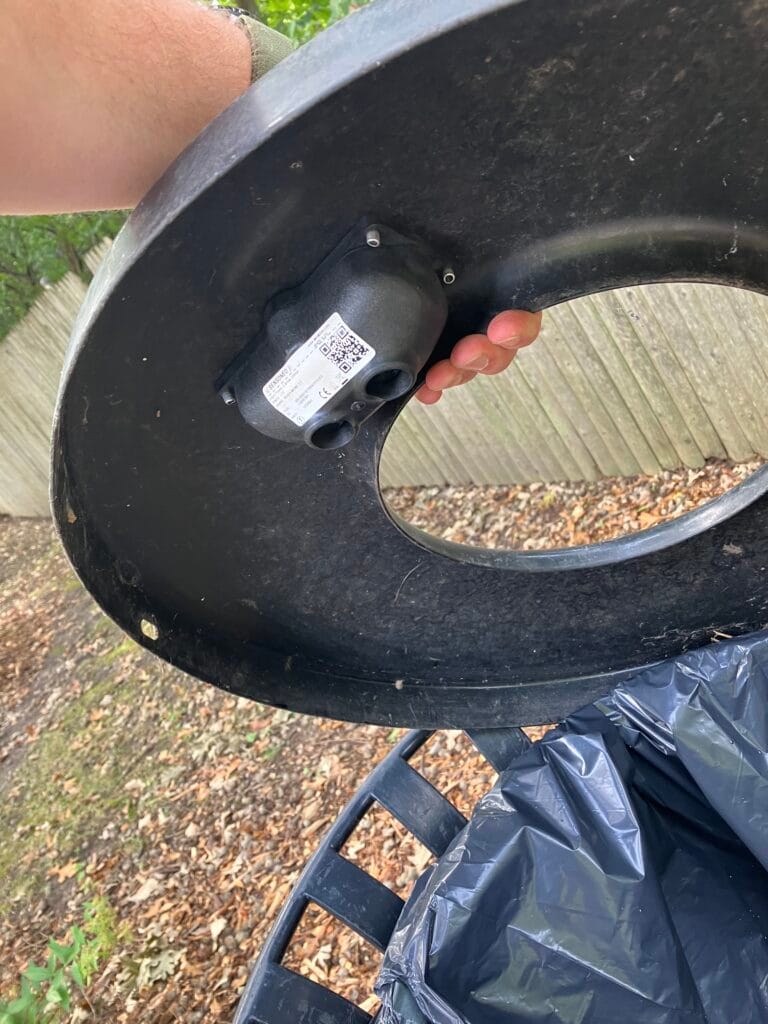 A person lifts a trash bin lid, showing a small sensor device mounted underneath.