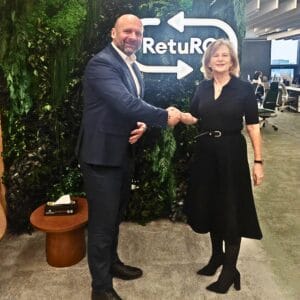 Two people shake hands in an office space with a green wall and “RetuRO” signage behind them.