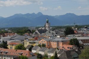 Colorful town buildings with a tall clock tower, backed by large green mountains.