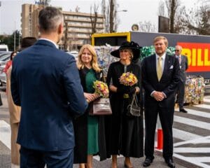 The Slovak president and a group of others stand near  recycling bales, listening to someone speak. 