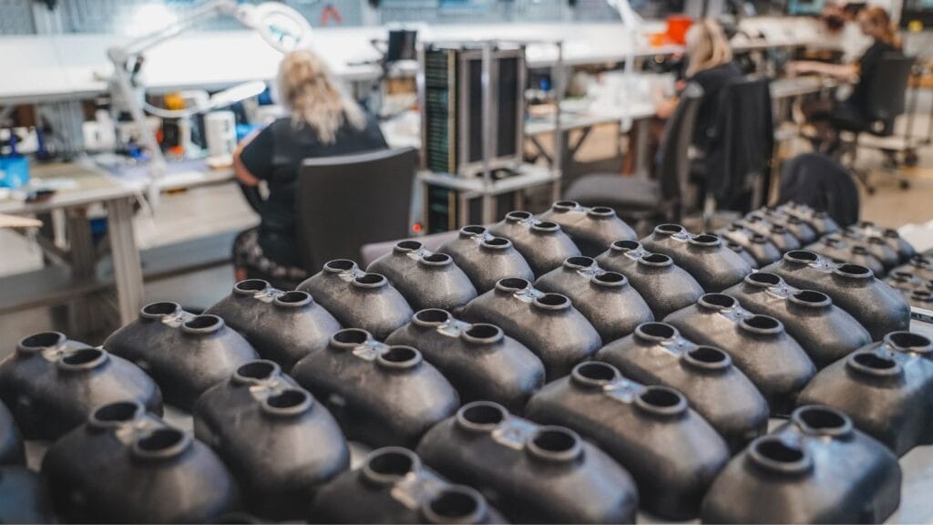 Rows of sensor housings lined up in a workshop where technicians assemble electronics.