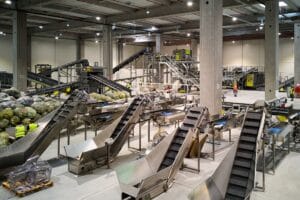 A large industrial sorting facility with multiple conveyor systems and workers handling bagged recyclables.