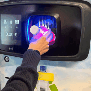 Hand inserting a plastic bottle into a glowing reverse-vending recycling machine with display screen.