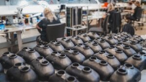 Rows of identical black plastic sensor components on a table in a workshop with workers assembling parts.