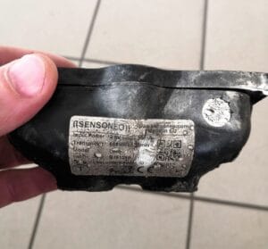 Burned and deformed Sensoneo sensor with melted casing and damaged label visible.