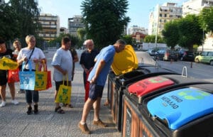 People recycling at color-coded outdoor bins during a community waste-sorting activity.