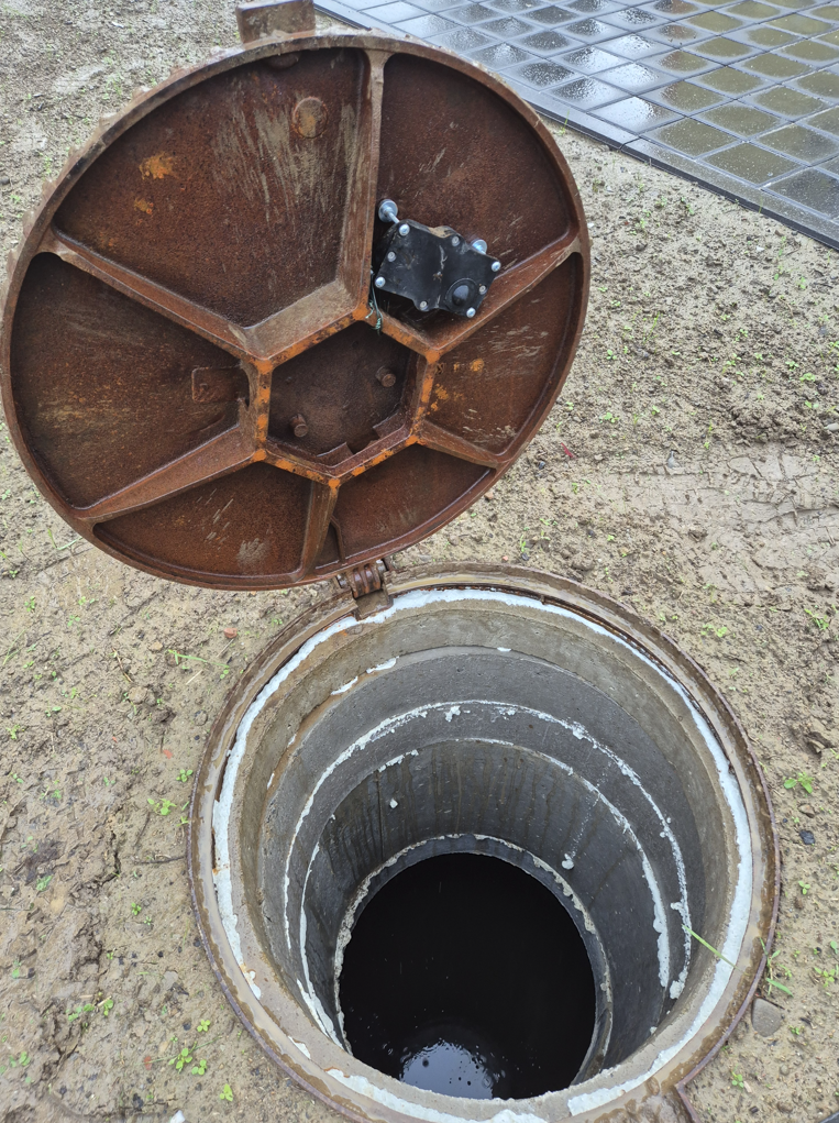 Black sensor unit bolted to the underside of the manhole cover.